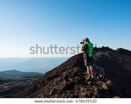 tourist photographer take a panoramic picture of the beautiful valley of Etna Vulcano with, craters, vegetation and lava stone during an excursion . satured color filter