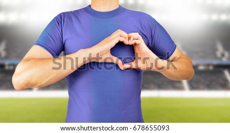 man making the heart shape with his hands over his chest in concept of love for football and soccer team at stadium in background.Concept of love to a team or colors in sport.