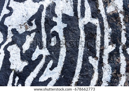 View of the surface of large stone covered with two colors of paint. Oil paints on grunge textured stone wall. Abstract backdrop with black and white lines, shapes, figures. Full filled frame picture.