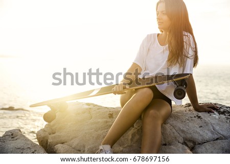 Beautiful and fashion young woman posing at the sunset with a skateboard 