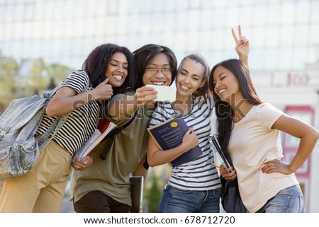 Image of multiethnic group of young happy students standing outdoors make selfie by phone. Looking aside.