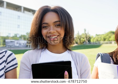 Picture of cheerful african student woman standing outdoors. Looking at camera.