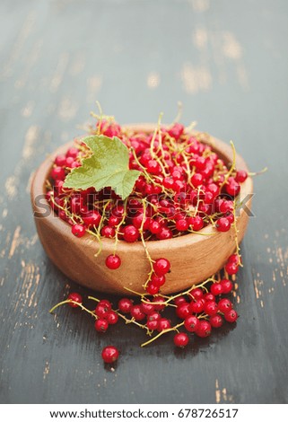 Juicy berries of red currant in a wooden round plate on a dark surface, closeup
