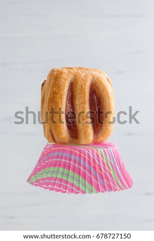 A pleasant and fun image of a fruit filled danish sitting on a cupcake paper. A grey, white wooden background. Vertical with copy space.