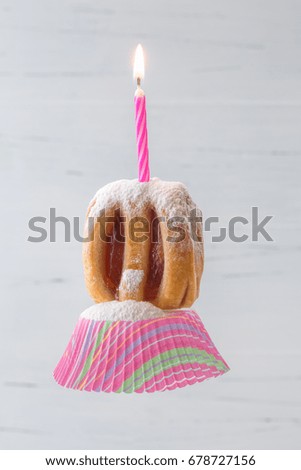 A pleasant and fun image of a fruit filled danish sitting on a cupcake paper with sprinkled powdered sugar and one lit candle. A grey, white wooden background. Vertical with copy space.