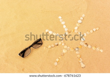 abstract sun image made of seashells on a sand with sunglasses