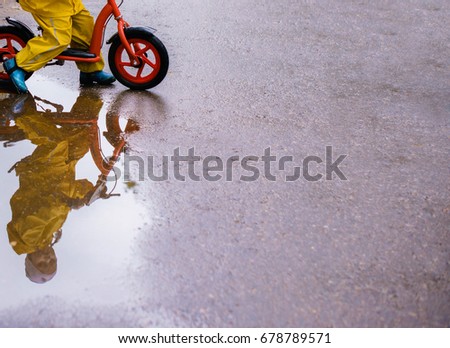 Little girl in yellow waterproof clothes with bike near a puddle