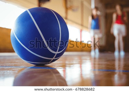 Close up of blue basketball on floor with female players in background