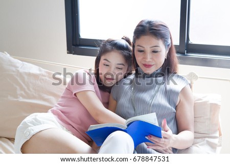 Smiling mother and daughter  are reading a book on bed home. Learning to read at home.