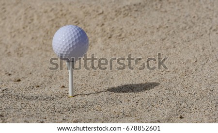 A golf ball on the tee, on the sand.