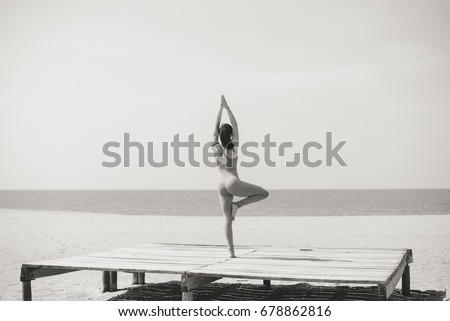 Attractive fitness woman stretching at the beach sunny outdoors copyspace background. Back view of sporty pretty lady keeping healthy wellbeing physical lifestyle. Black and white picture