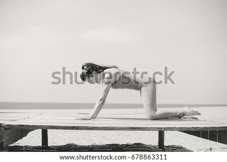 Attractive fitness woman stretching at the beach sunny outdoors copyspace background. Back view of sporty pretty lady keeping healthy wellbeing physical lifestyle. Black and white picture