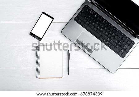 Top view on white wooden table with open blank laptop computer, cell phone, and empty diary with pen, free space. Mobile phone with white screen, copy space 