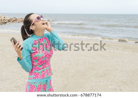 A beautiful asian (thai) woman is listening to music And exercise with feeling happy on the beach and stone copy space