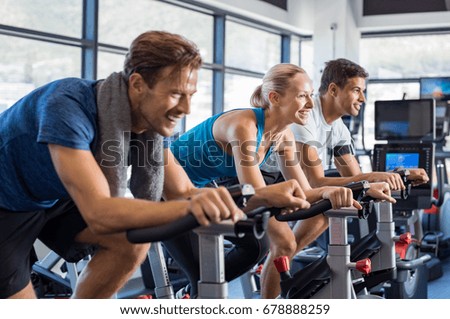 Group of smiling friends at gym exercising on stationary bike. Happy cheerful athletes training on exercise bike. Young men and woman working out at a class in the gym. Royalty-Free Stock Photo #678888259