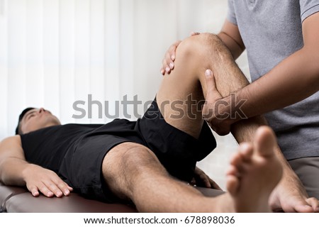 Therapist treating injured knee of athlete male patient in clinic - sport physical therapy concept Royalty-Free Stock Photo #678898036