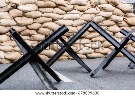 Black steel street barrier in shape of anti-tank Czech hedgehog obstacle defense stands on asphalt urban road.