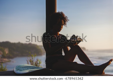 Beautiful surfer girl reading book at sunset on the beach in Bali, Indonesia. copy space