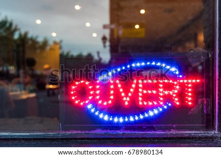French ouvert open sign for store shop or restaurant glowing in the evening with window reflection