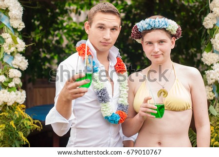 a guy and a girl on a Hawaiian party, a wreath and a necklace, drink a green drink.