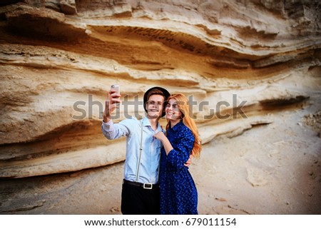 Attractive man with a beautiful woman are hugging and smiling. They are making selfie on the background of sand quarry.
