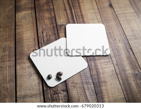 Blank square beer coasters and coffee beans on vintage wooden table background. Responsive design mockup.