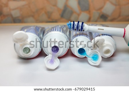 Four open tubes of toothpaste on a white surface and a toothbrush in the bathroom. Different types and colors of toothpaste. Royalty-Free Stock Photo #679029415