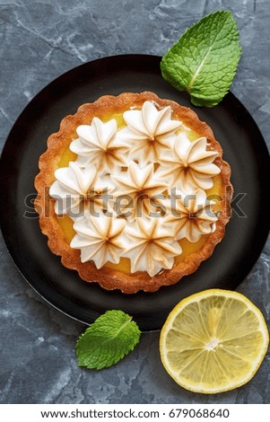 Plate with lemon tartlet, mint leaves and lemon slices on gray background.