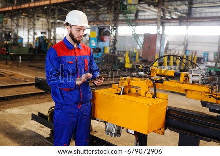 Man working in a construction helmet with a tablet on the background of a plant