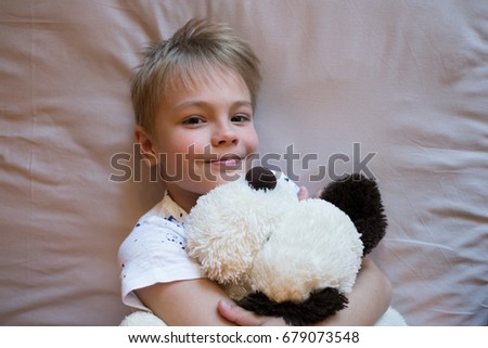portrait of happy small boy lies on the bed with toy and smiling.