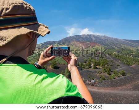 tourist photographer take a panoramic picture, with his smarphone, of the beautiful valley of Etna Vulcano with, craters, vegetation and lava stone during an excursion .