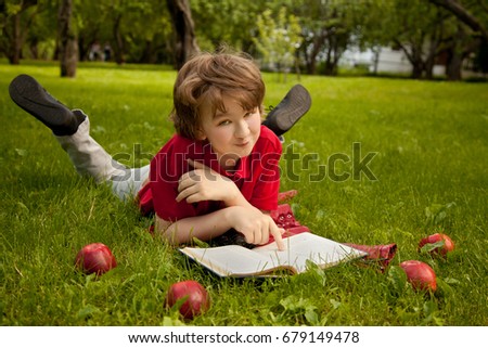 teen boy reading a book in the green summer apple trees park