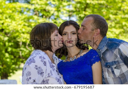 Parents kiss their adult daughter in both cheeks.