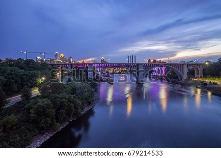 A Wide Angle Long Exposure Shot of the Colorful 10th Ave, 35W, and Stone Arch Bridges Spanning the Mississippi River and Downtown Minneapolis in the Background during a Summer Twilight Hour