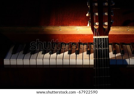 Closeup of guitar standing near open piano on dark background with lighting effect