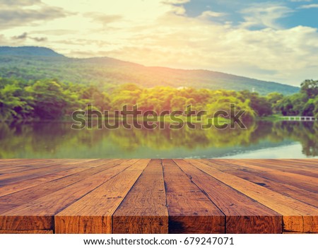 vintage tone image of old wooden table and the lake with rainy sky and mountain in background.