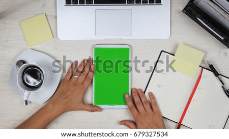 woman using a mobile phone / tablet PC with green screen at her desk in the office - top view