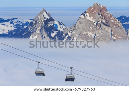 Chair lift on Mt. Fronalpstock in the Swiss canton of Schwyz, summits of the Kleiner Mythen and Grosser Mythen mountains rising from sea of fog. The picture was taken in wintertime.