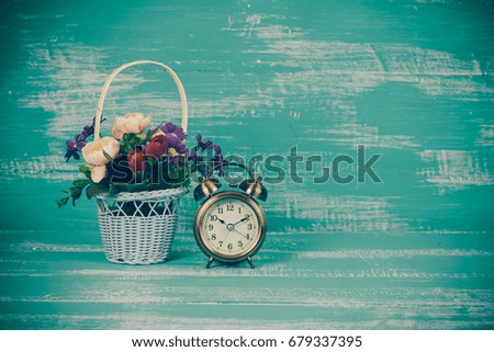 flower in basket with clock on wood background.
