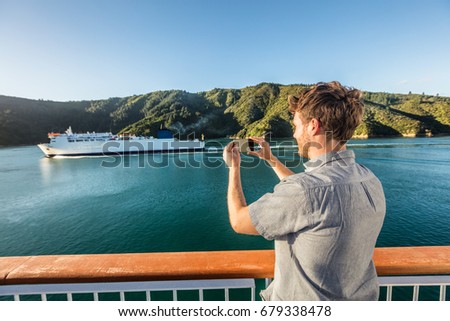 Cruise travel man tourist taking phone picture of ferry boat cruising on sea. Tourism photos during New Zealand island crossing holiday at Marlborough sounds Cook strait.