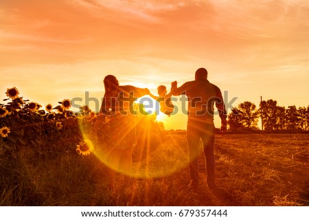 Happy family dad pregnant mom playing in the fresh air on the field near the sunflowers watching the beautiful emotional sunset in the backlight