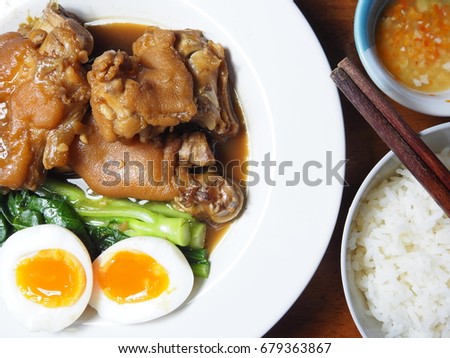 Top view picture of stewed pork leg, boiled chinese kale, boiled egg and rice on white plate above wooden table.