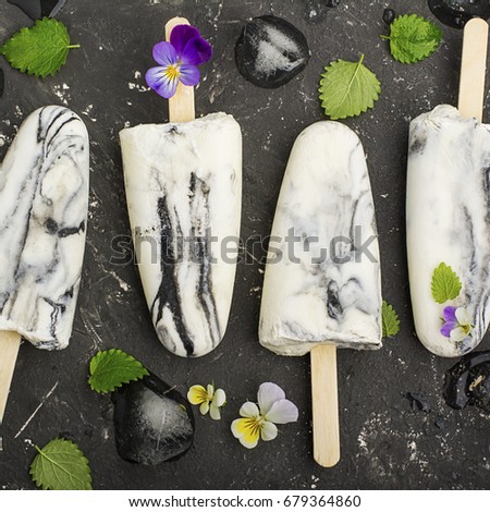 Yoghurt refreshing marble ice cream popsicle in trendy fashion colors on a dark background with edible flowers of garden violas. Selective focus. Top View.