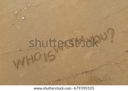 Handwriting  words "WHO IS WITH YOU?" on sand of beach.