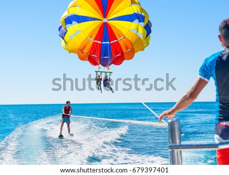 Happy couple Parasailing in Dubai beach in summer. Three people rest on the sea. Parachute and water skiing. Royalty-Free Stock Photo #679397401