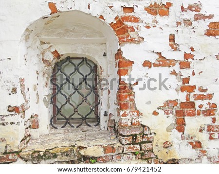 Forged medieval window with a lattice on the background of an old brick wall and white cracked paint. Ancient window in the monastery.