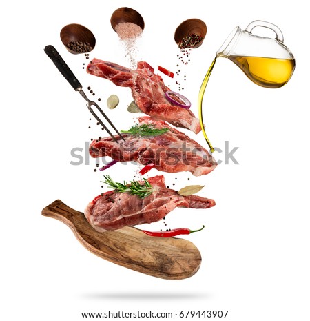 Flying pieces of raw pork steaks, with ingredients for cooking, served on woodenboard. Concept of food preparation in low gravity mode. Separated on white background. High resolution image