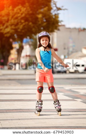 Cute little girl learning to roller skate in city skate park on beautiful summer day.