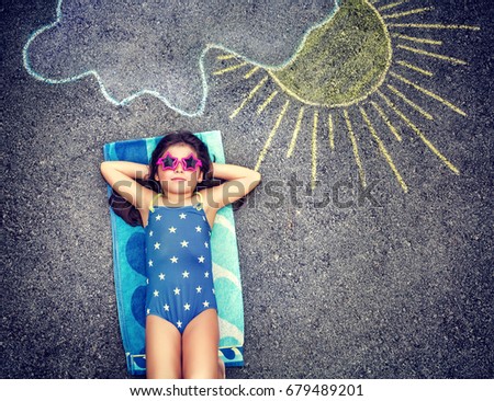 Happy little girl wearing swimsuit and lying down on the asphalt near picture of the sun comes out from behind the clouds, cute baby needs of summer holidays