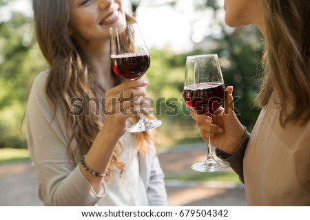 Cropped picture of young two women outdoors in park drinking wine.